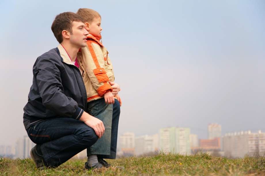 Father and young son looking out over city skyline from park.