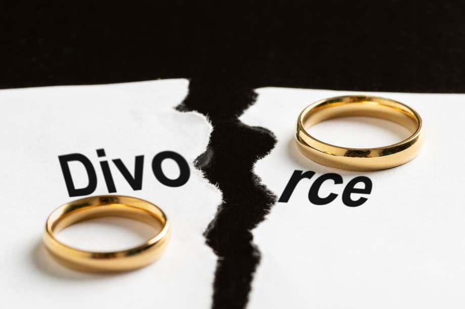 Two gold wedding rings rest on a piece of paper torn through the word divorce.