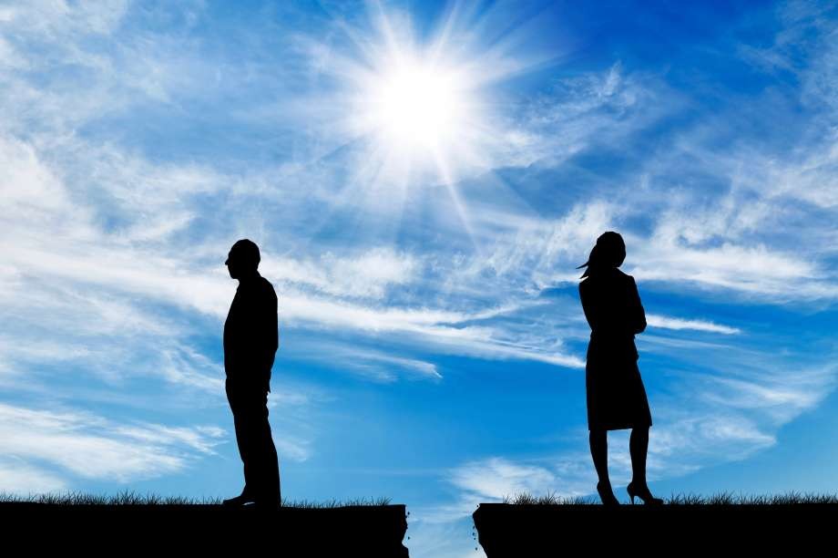 Silhouette of a man and woman standing apart on cracked ground.