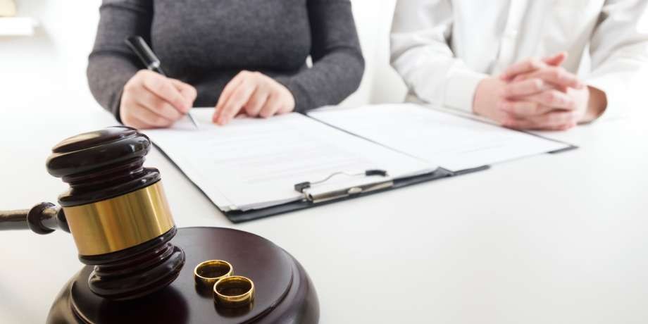 Close-up of a person signing legal divorce papers near a judge's gavel.