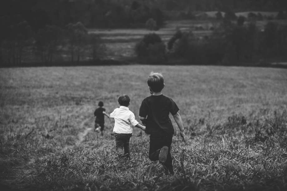 A black and white photo of three children running through an open field.