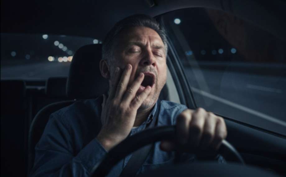 A tired man yawns while driving a car at night.