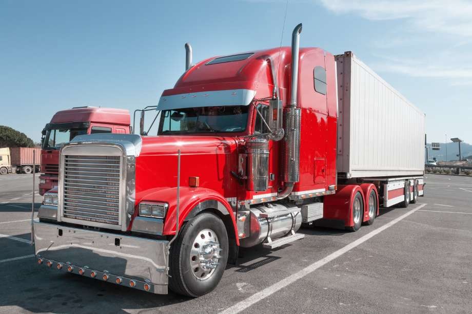 Large red semi-truck with a white trailer parked in a commercial lot.
