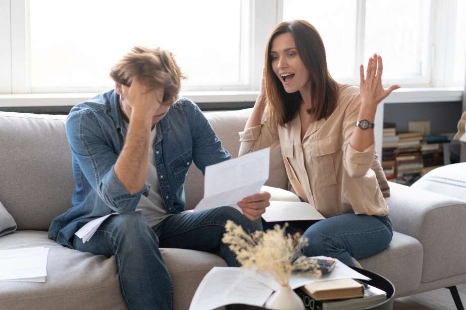 A frustrated couple arguing over legal documents while sitting on a couch.