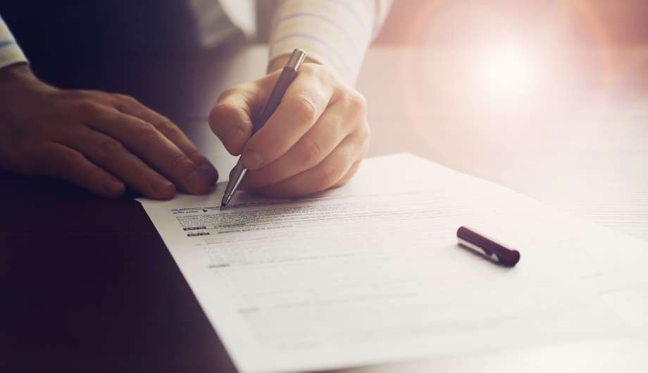 Close-up of a hand signing a legal contract with a pen in warm light.