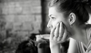 Black and white photo of a woman in profile resting her chin on her hand, looking thoughtfully into the distance, capturing the quiet contemplation seen during emotional distress claims amid COVID-19 in Brooklyn NYC.