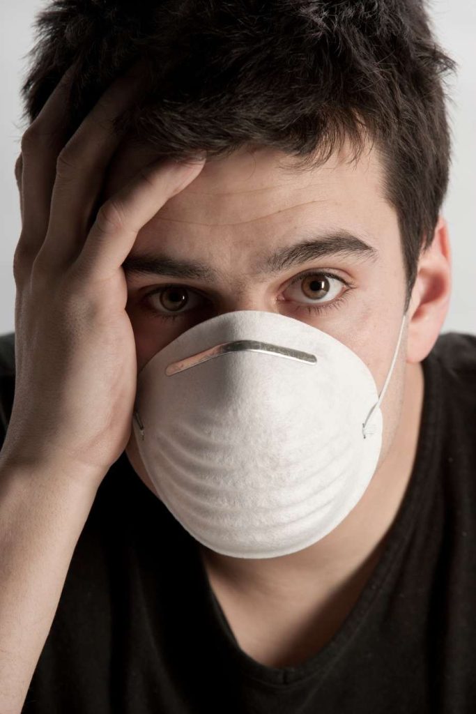 Young man wearing a protective dust mask while holding his head.
