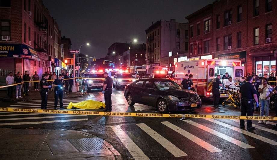 Police and emergency responders are at a nighttime crime scene on a city street following a hit and run accident in NYC, with a covered body, police tape, and emergency vehicles present.