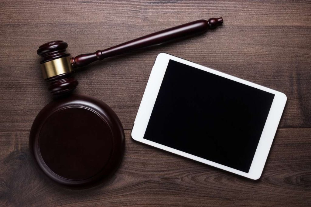Wooden judge gavel resting next to digital tablet on dark desk.