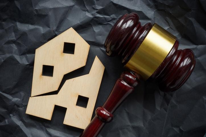 A wooden judge's gavel resting next to a broken wooden house model.