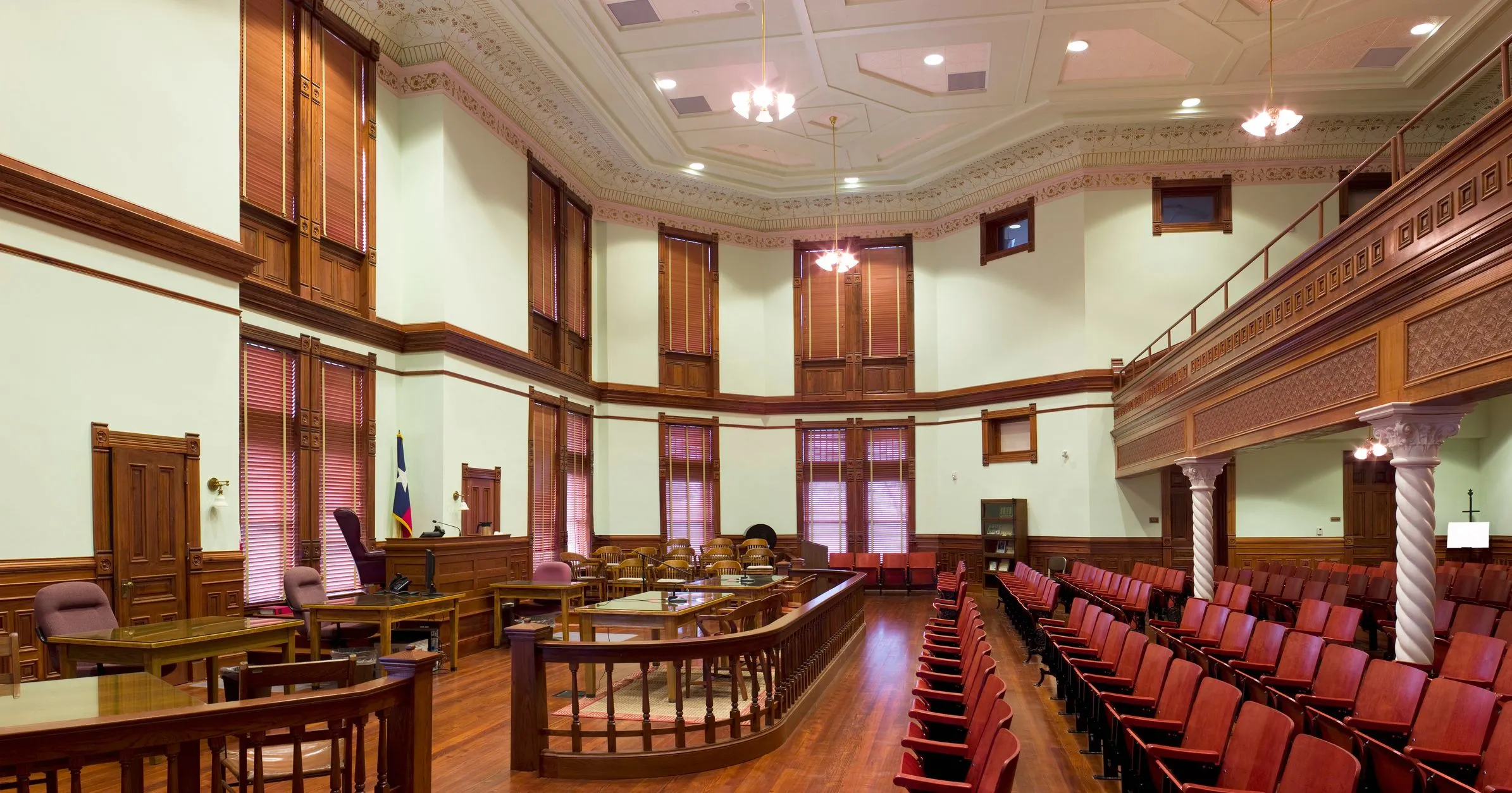 Large historic courtroom with ornate wood trim and red gallery seating.
