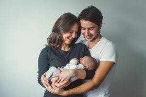 Smiling parents holding their newborn baby together in a bright room.