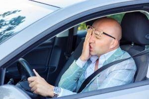 Man in a suit holding his face in pain while driving a car.