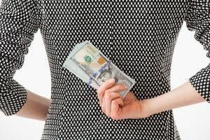 A person in a patterned dress hides a large stack of cash behind their back.