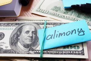A stack of hundred-dollar bills secured with a rubber band and a blue note labeled "alimony."