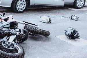 A motorcycle lies on its side next to a fallen helmet and vehicle parts on the road near a parked car, suggesting an accident scene—raising the question: What Are Common Causes of Motorcycle Accidents in New York?.