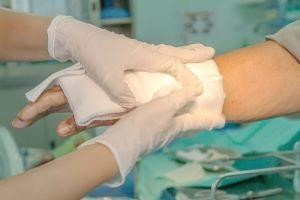 A healthcare professional wearing white gloves applies a clean gauze bandage to a patient's arm.