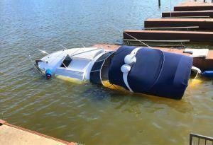 A partially sunken boat with a blue cover is submerged in water near a dock, raising the question: What if I am injured in a boating accident in New York?.