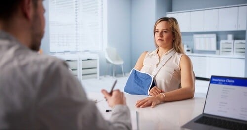 woman wearing arm sling meeting with attorney reviewing insurance claim laptop