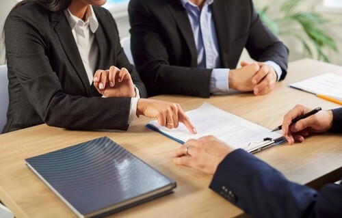 two professionals in suits reviewing and pointing at legal document across desk